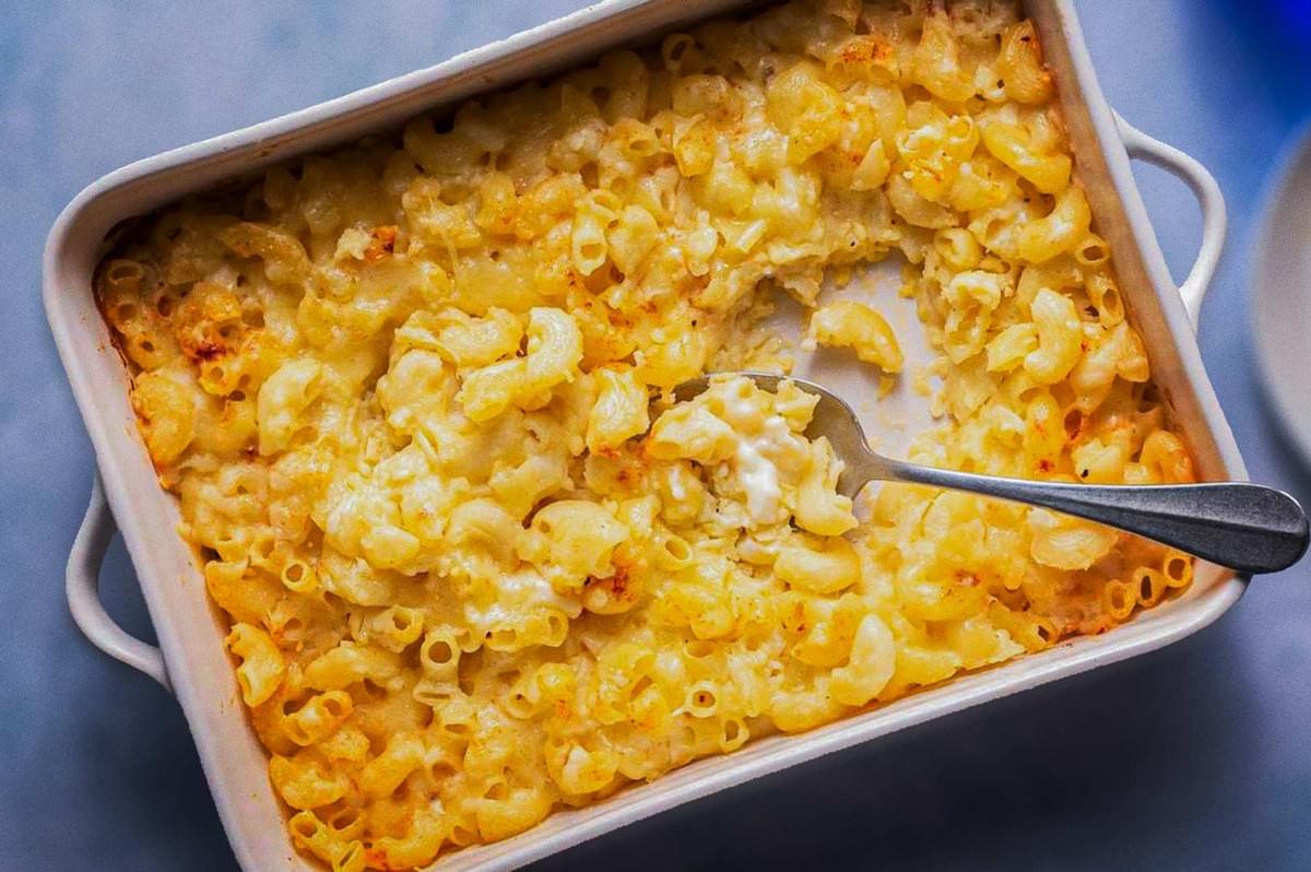 American baked macaroni and cheese in white ceramic dish, golden melted topping with crispy edges, fork inside creamy pasta.