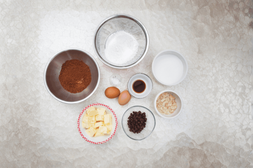 A neatly arranged set of brownie ingredients—flour, cocoa, eggs, butter, and more—ready for either fudgy or cakey technique.