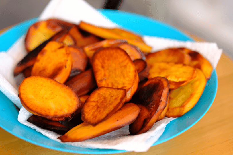 A blue bowl lined with paper towels filled with roasted, golden-brown sweet potato medallions, showing caramelized edges and a crispy texture.