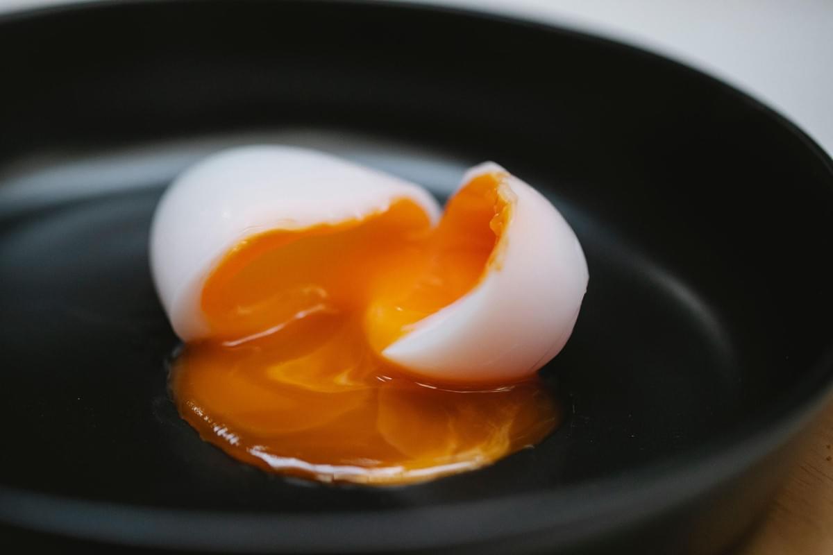 A soft-boiled egg is split open in the center of a black dish. Bright, runny yellow yolk spills out from the firm white egg white onto the surface.