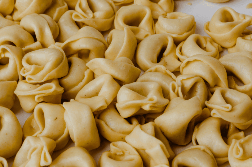 A pile of fresh, uncooked tortellini, the classic ring-shaped stuffed pasta native to the Emilia-Romagna region.