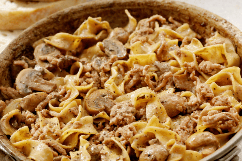 A rustic, close-up view of a shallow dish completely filled with comforting Russian Beef Stroganoff, featuring tender meat, mushrooms, and egg noodles coated in a rich sauce.