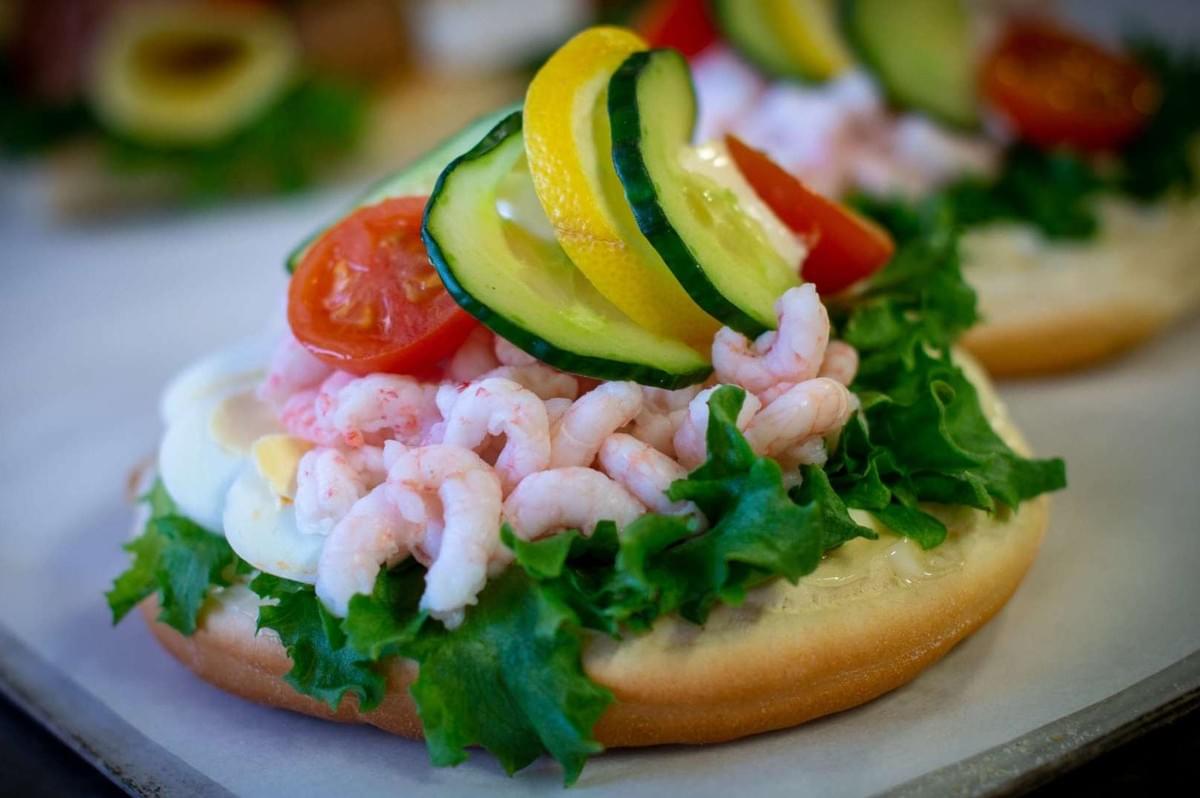 A close-up of a Räksmörgås, featuring shrimp, fresh cucumbers, and ripe tomatoes on a slice of bread.