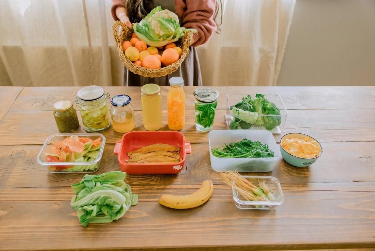 Person holding a basket of fresh produce above a table with organized meal-prep ingredients.