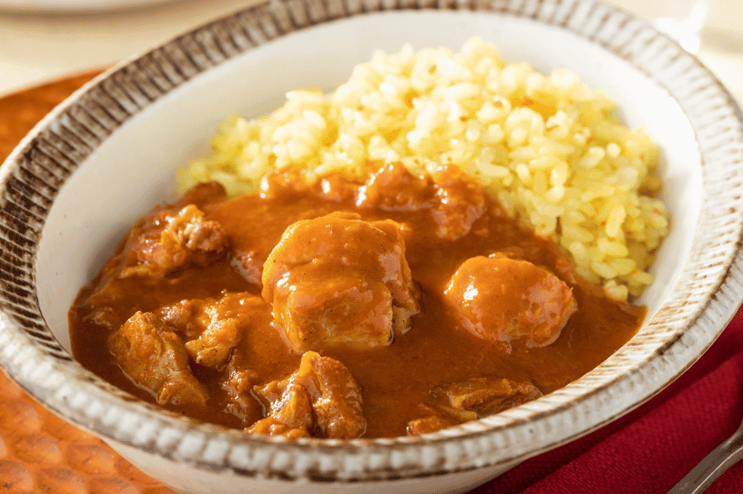 A rustic bowl of reddish-brown chicken curry paired with vibrant yellow rice—an inviting portrait of home-style Indian comfort food.