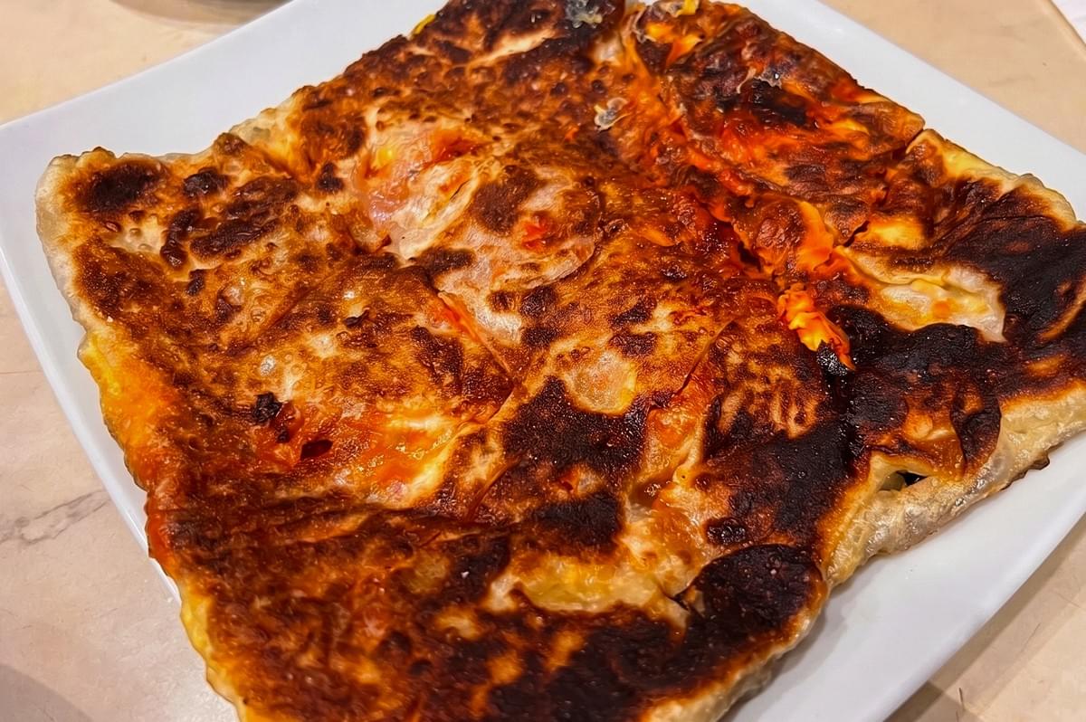 A plate of golden-brown murtabak with crispy edges served at a local eatery, highlighting the texture of the folded pastry.