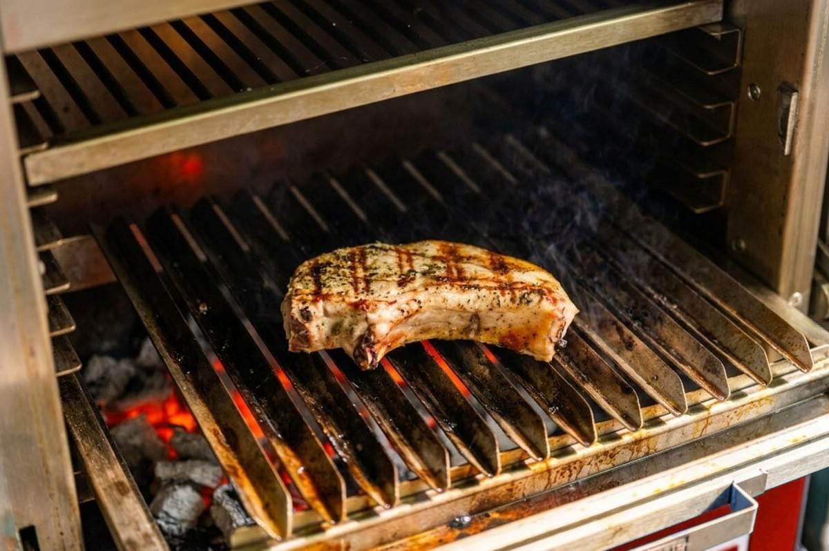 Grilled pork chop on metal grate over glowing embers