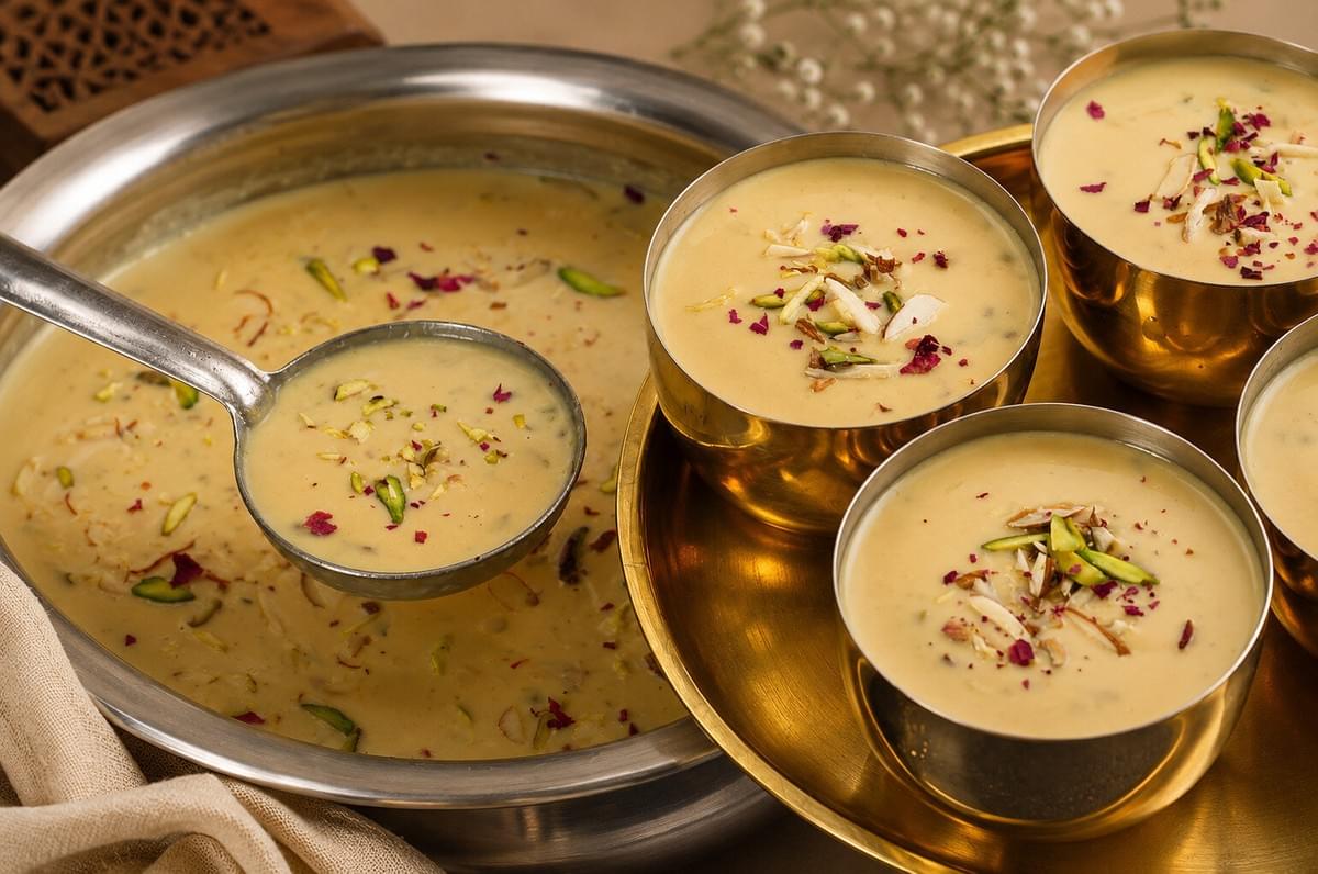 Ladle scooping creamy kheer from a large pot into small metal serving cups.