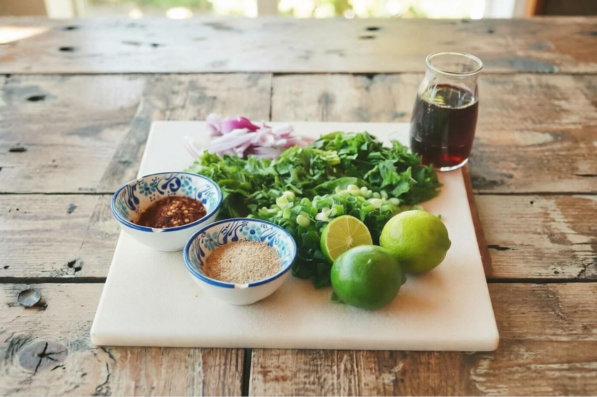 Fresh herbs, limes, shallots, and spices laid out on a board, ready to season Laotian Larb