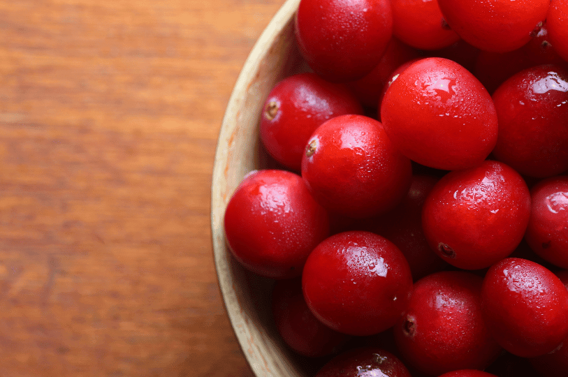 A close-up, artistic shot of a wooden bowl filled with vibrant, moist cranberries, highlighting the texture of the berries and the warm grain of the wood.