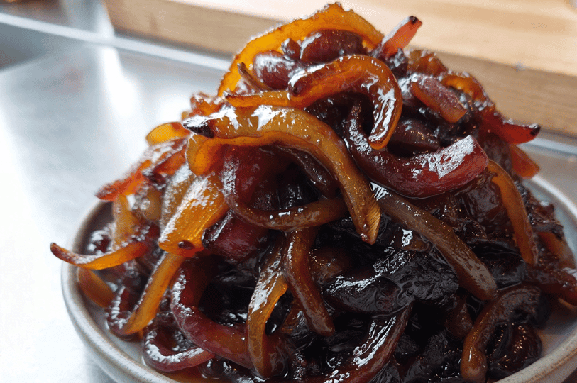A mound of glistening, mahogany-colored caramelized onions on a small white plate, showcasing the soft, tender consistency achieved through slow cooking.