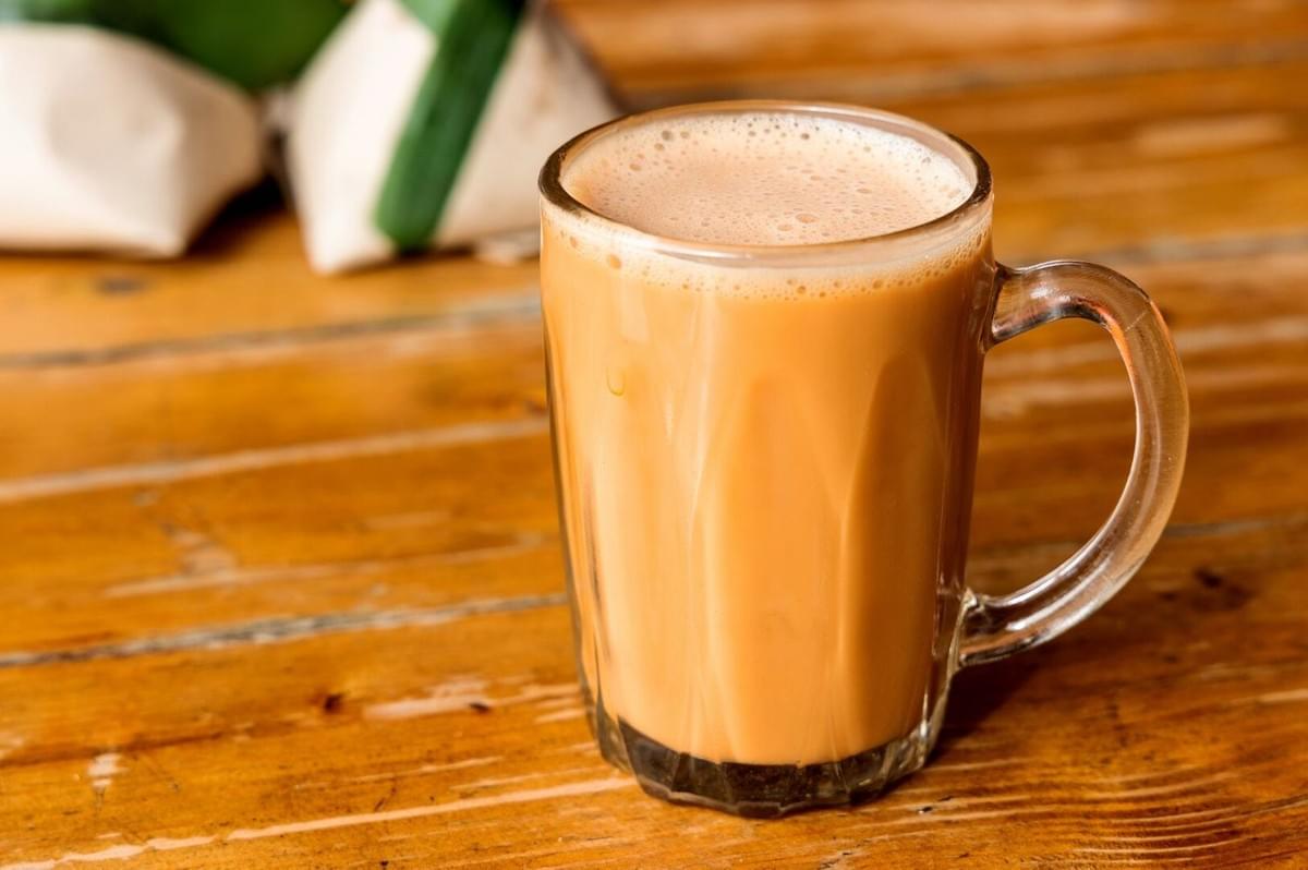 A glass of Teh Tarik coffee on a wooden table, showcasing the beverage's creamy texture and rich color.