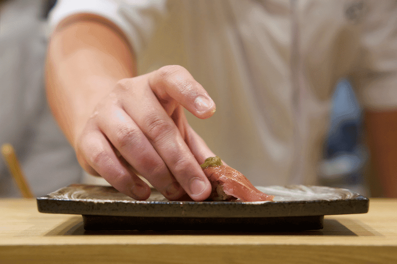 A chef’s hand gently places a garnished piece of sushi onto a ceramic plate, embodying the refined care and seasonal elegance found in Singapore’s authentic Japanese dining experiences.