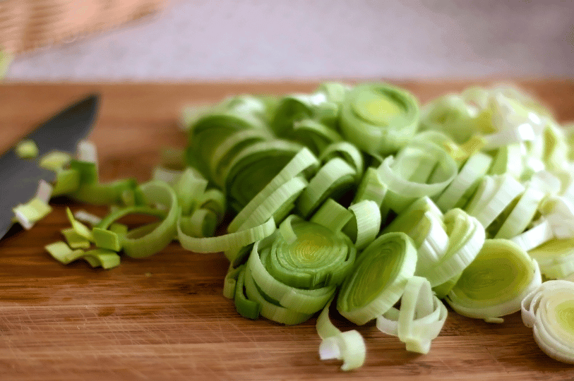 A pile of neatly sliced leek rings on a wooden chopping board, showcasing the beautiful internal circular layers.