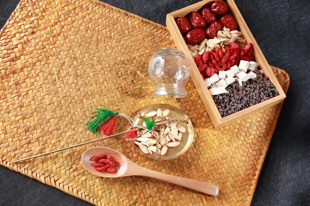 Traditional Chinese Medicine (TCM) ingredients including goji berries, red dates, and herbs with a vintage scale on a woven mat.