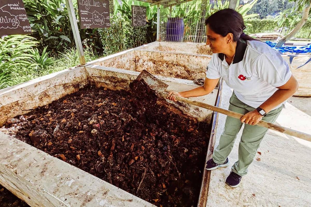 Person turning compost in an outdoor composting area.