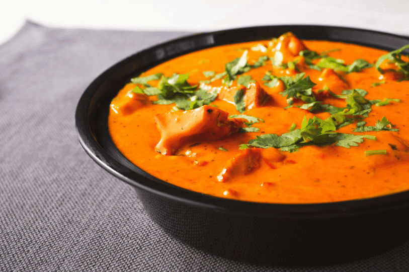 A bowl of Indian butter chicken in creamy tomato sauce, garnished with cilantro and served on a gray cloth—highlighting the dish’s rich color and comforting simplicity.
