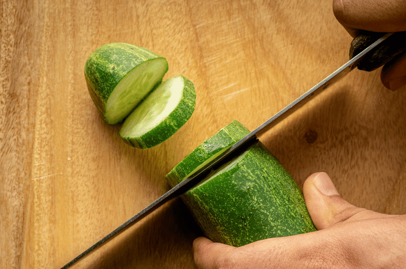 Freshly picked, whole green cucumbers with fresh water droplets resting in a woven garden basket under natural sunlight.