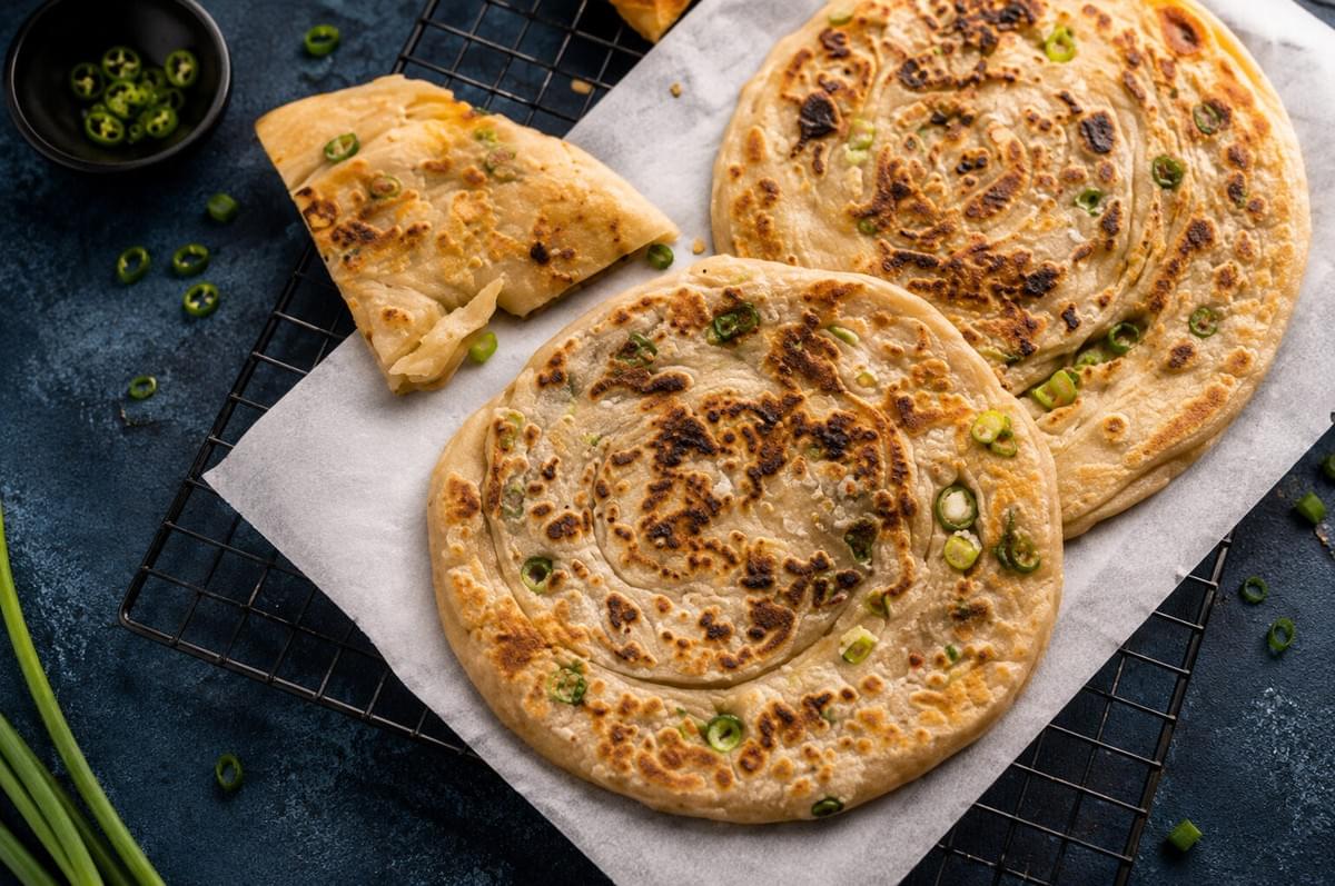 Crispy scallion pancakes served on parchment paper and a cooling rack with chopped green onions.
