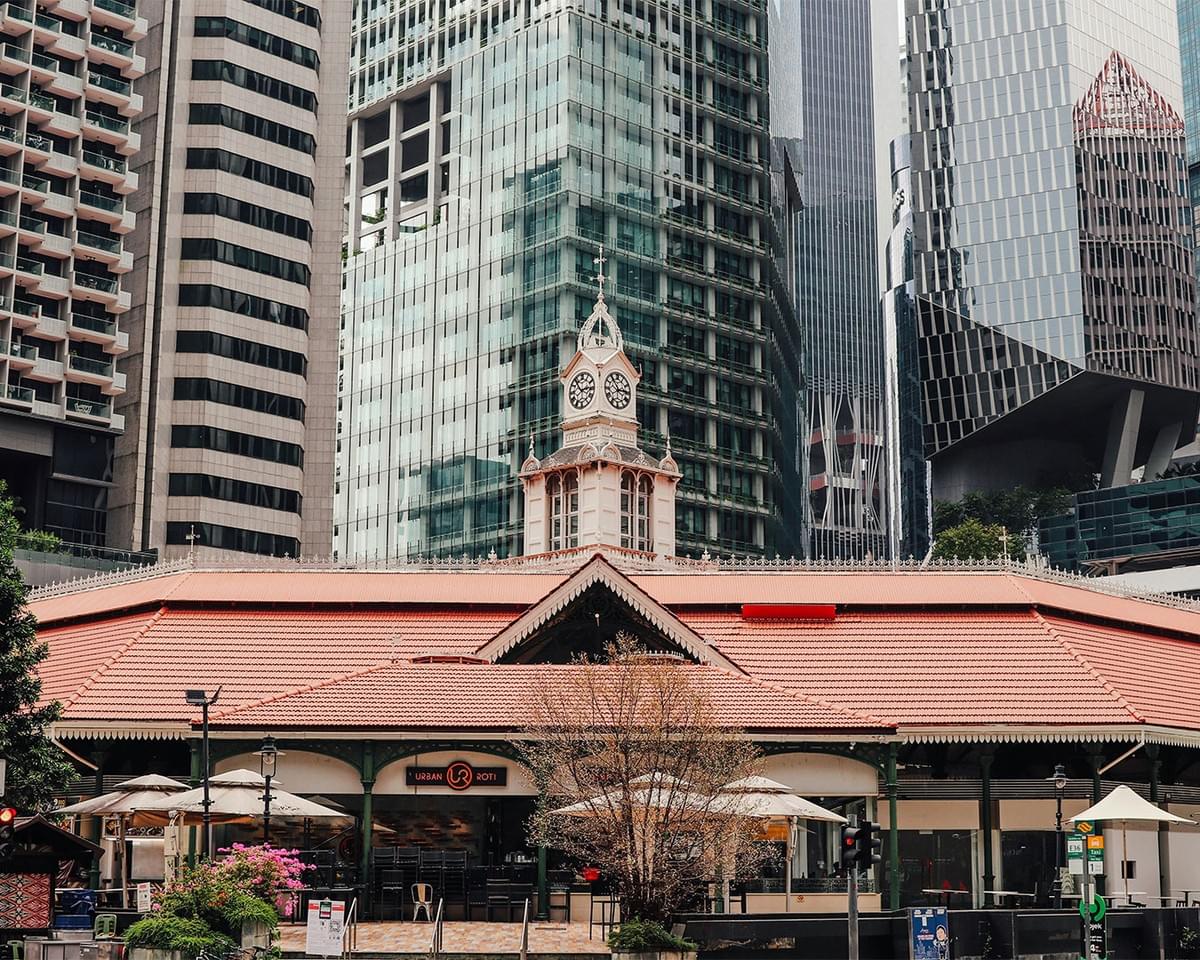 The exterior of Lau Pa Sat, a historic hawker centre in Singapore, featuring its distinctive Victorian-style iron structure surrounded by modern city buildings.