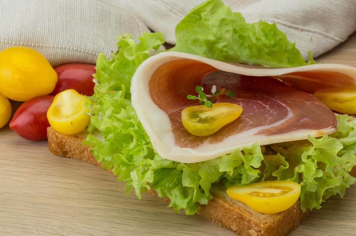 A Danish open sandwich topped with assorted meats and vibrant vegetables on a slice of bread.