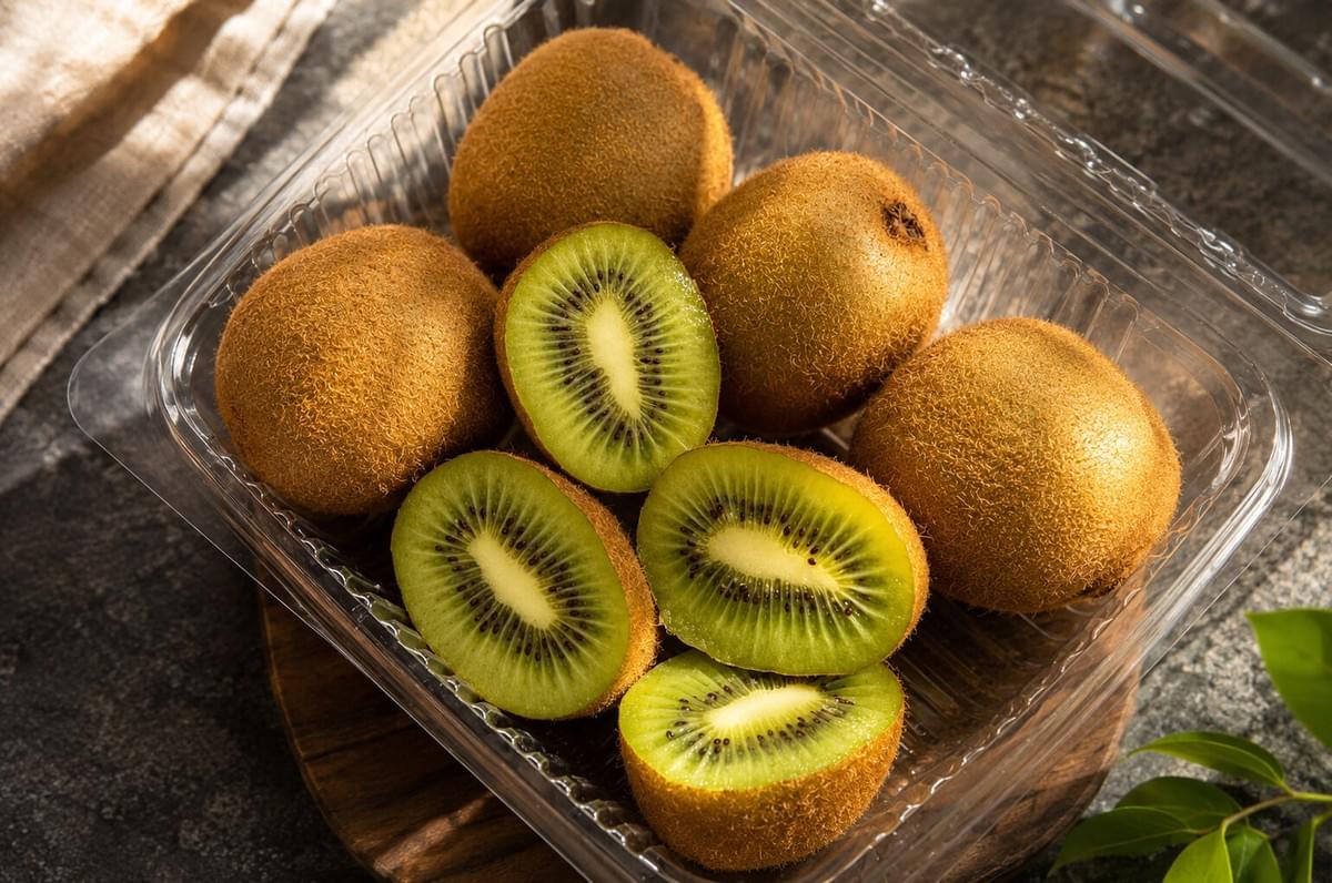 Clear plastic container filled with whole and halved fresh green kiwifruits.