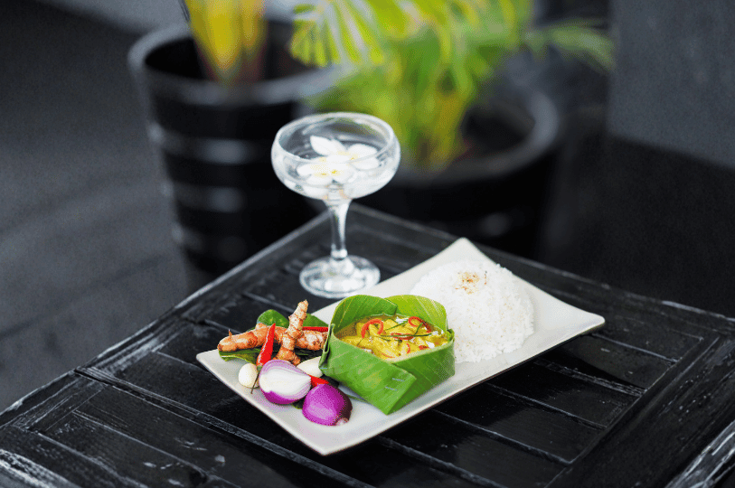 A close-up of rich yellow Cambodian amok served inside a rustic, hollowed-out coconut shell, garnished with thick coconut cream and green herbs, sitting on a large green banana leaf.