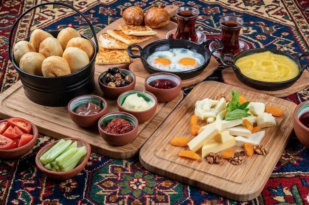 Authentic Turkish kahvalti spread on a patterned rug with bread rolls, fried eggs, cheeses, honey, olives, and traditional tea glasses
