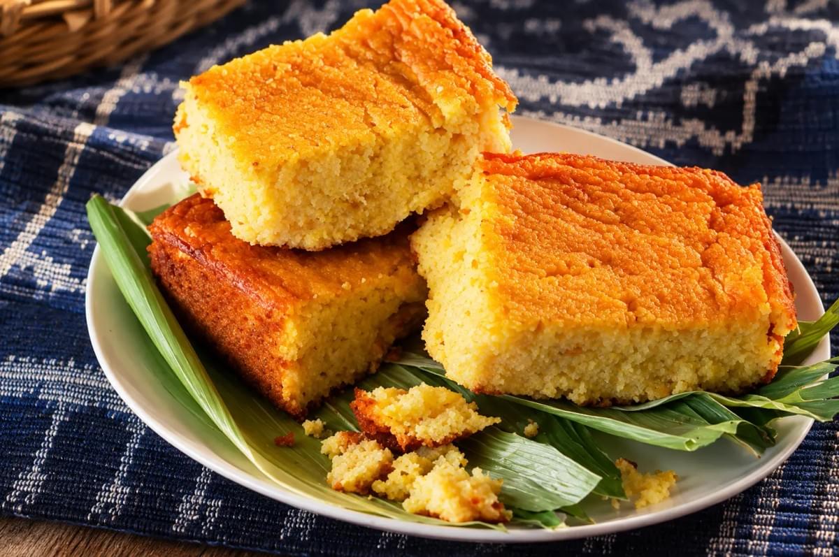 Three thick slices of golden cornbread stacked on a plate with green leaves.