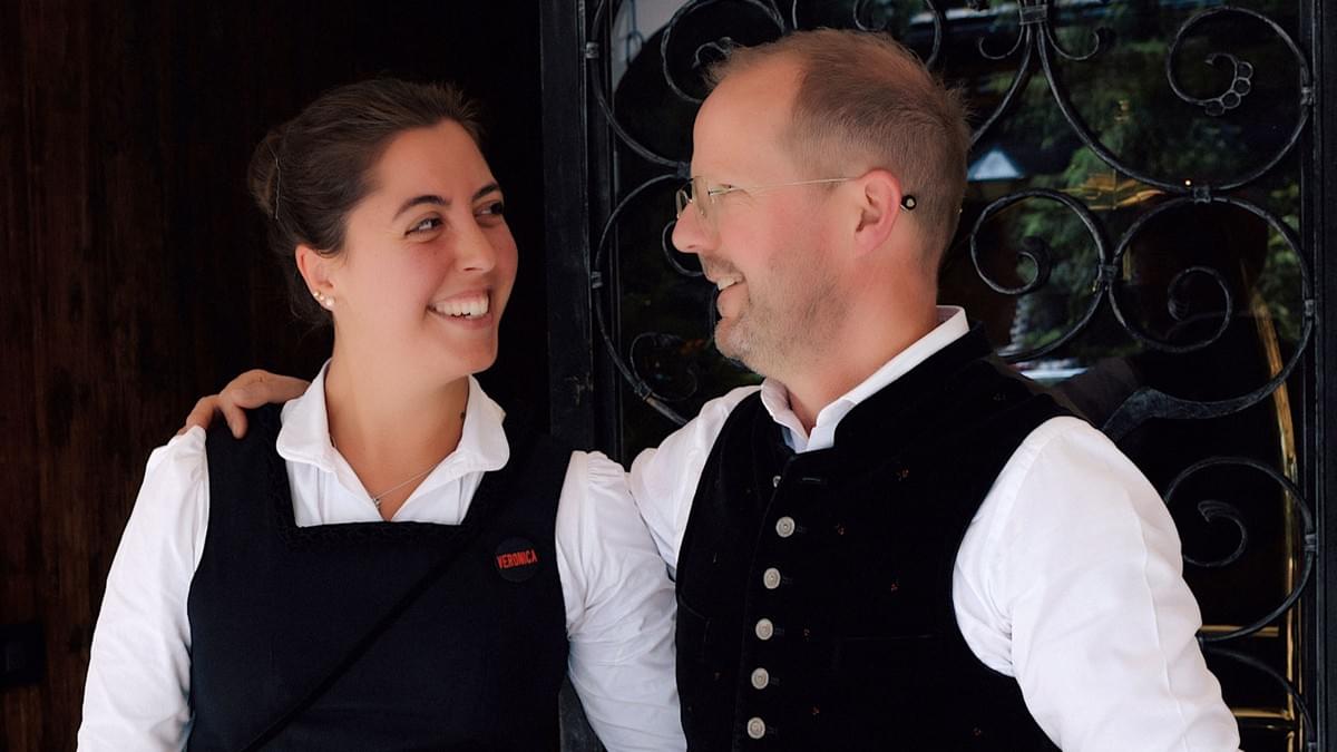 Eine Mitarbeiterin und ein Mitarbeiter eines Hotel stehen nah bei einandern und lächeln sich an