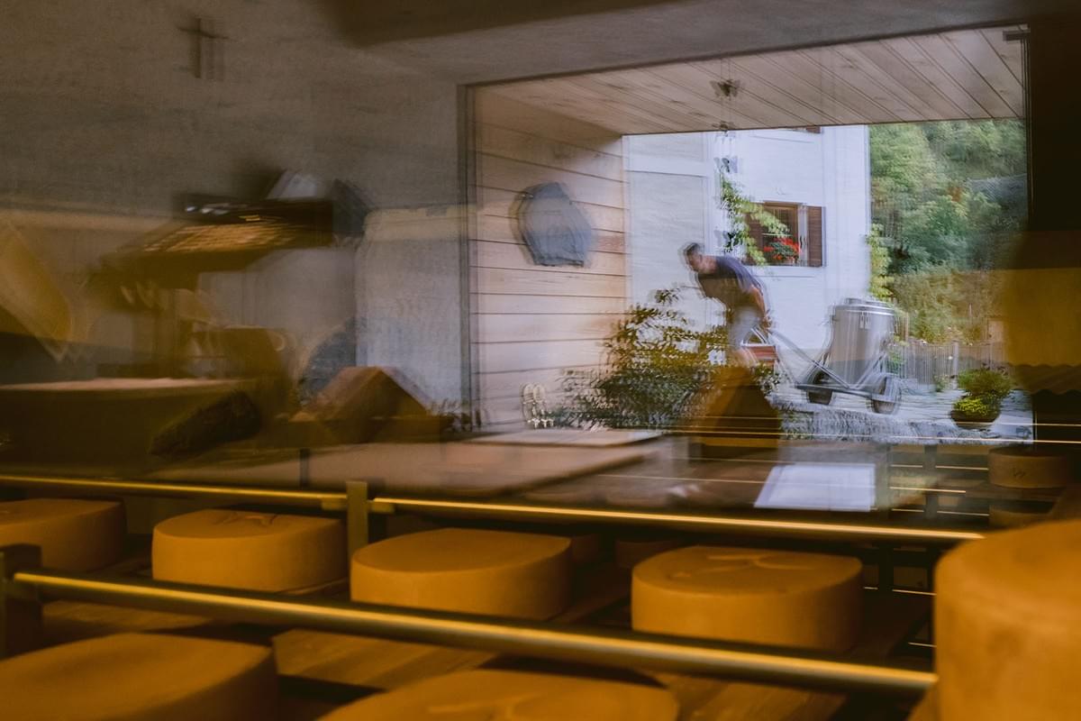 Spiegelung in einer Scheibe, hinter der Scheibe Käseleibe, in der Spiegelung der Bauer mit Milchkanne