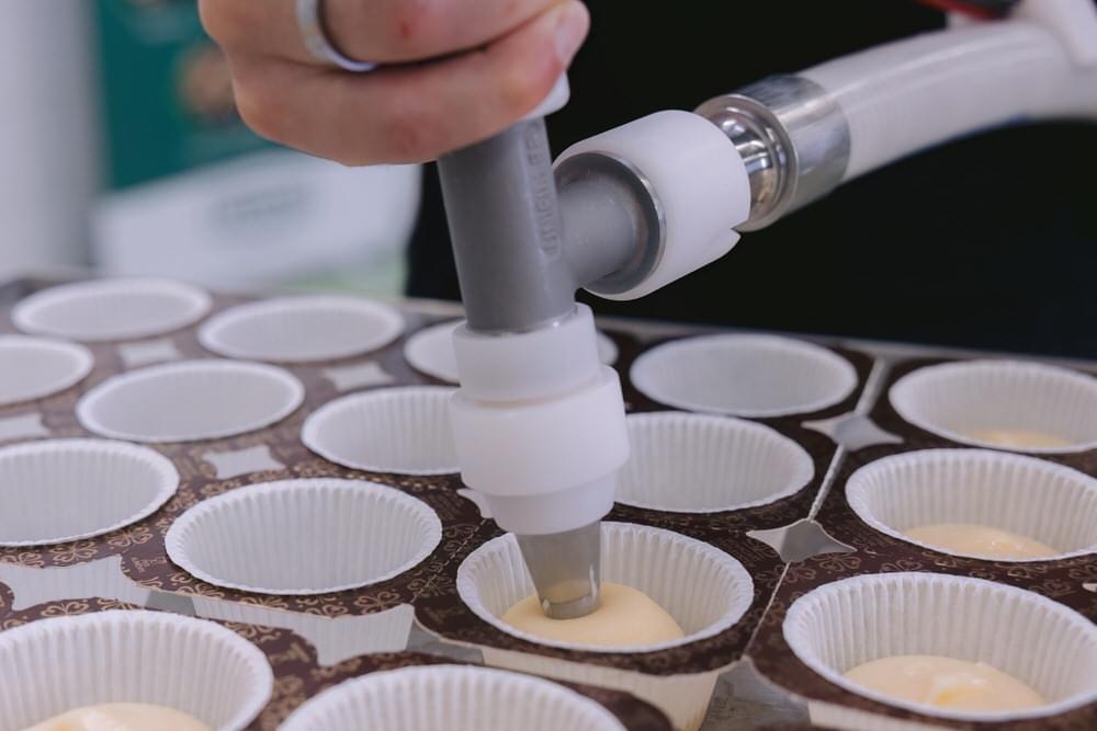 Ein Mann füllt Teig mit einem Füllkopf in Muffinformen