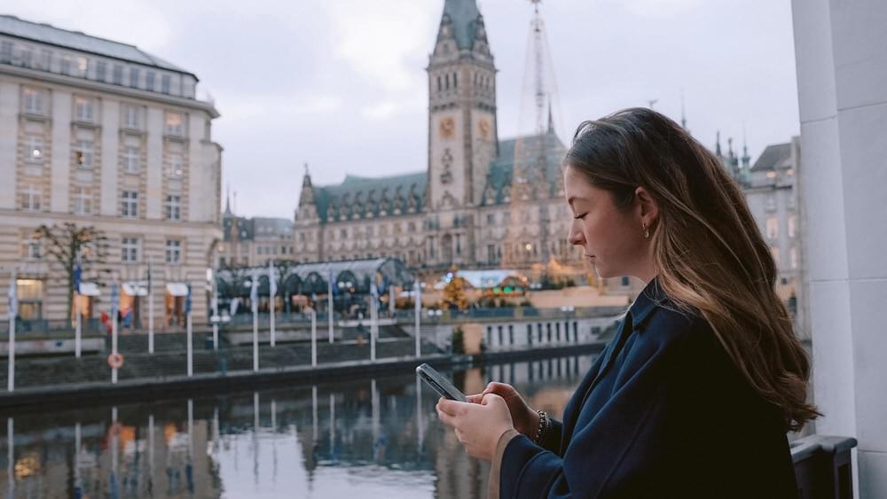 Eine junge Frag guckt auf ihr Handy, im Hintergrund das Hamburger Rathaus
