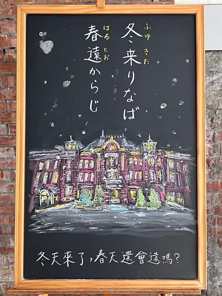 小さい黒板にチョークで絵が描いてあります。日本語のことわざを紹介するための絵です。上部に縦書き二行で「冬来りなば春遠からじ」とあり、その下に、雪が降りしきる東京駅のイラストが描いてあります。レンガ造りの建築物です。