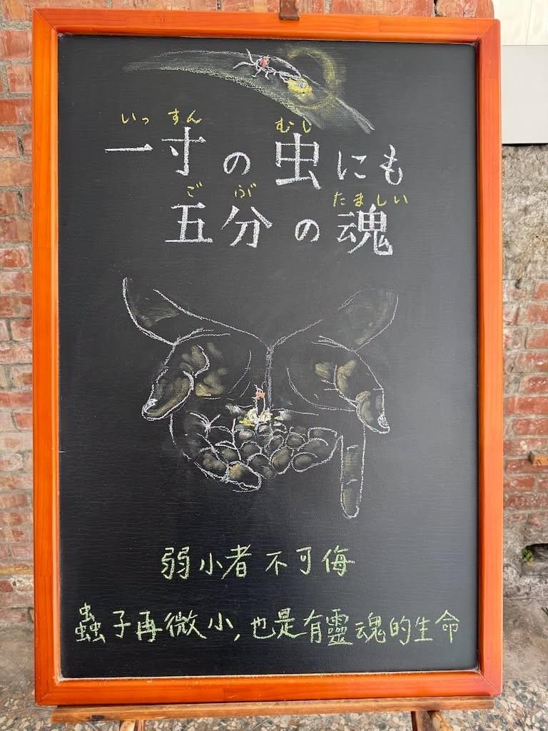 小さい黒板にチョークで絵が描いてあります。日本語のことわざを説明するための黒板です 縦長の黒板で、上部に葉っぱに止まった蛍のイラストが描いてあります。蛍はお尻が光っています。 その下に横書きで「一寸の虫にも／五分の魂」と書いてあります。その下に大きく、人の手のイラストが描いてあります。両手を揃え、何かを包みこんでいるような形です。手のくぼみの中に小さな虫、蛍がいて、小さく光っています。