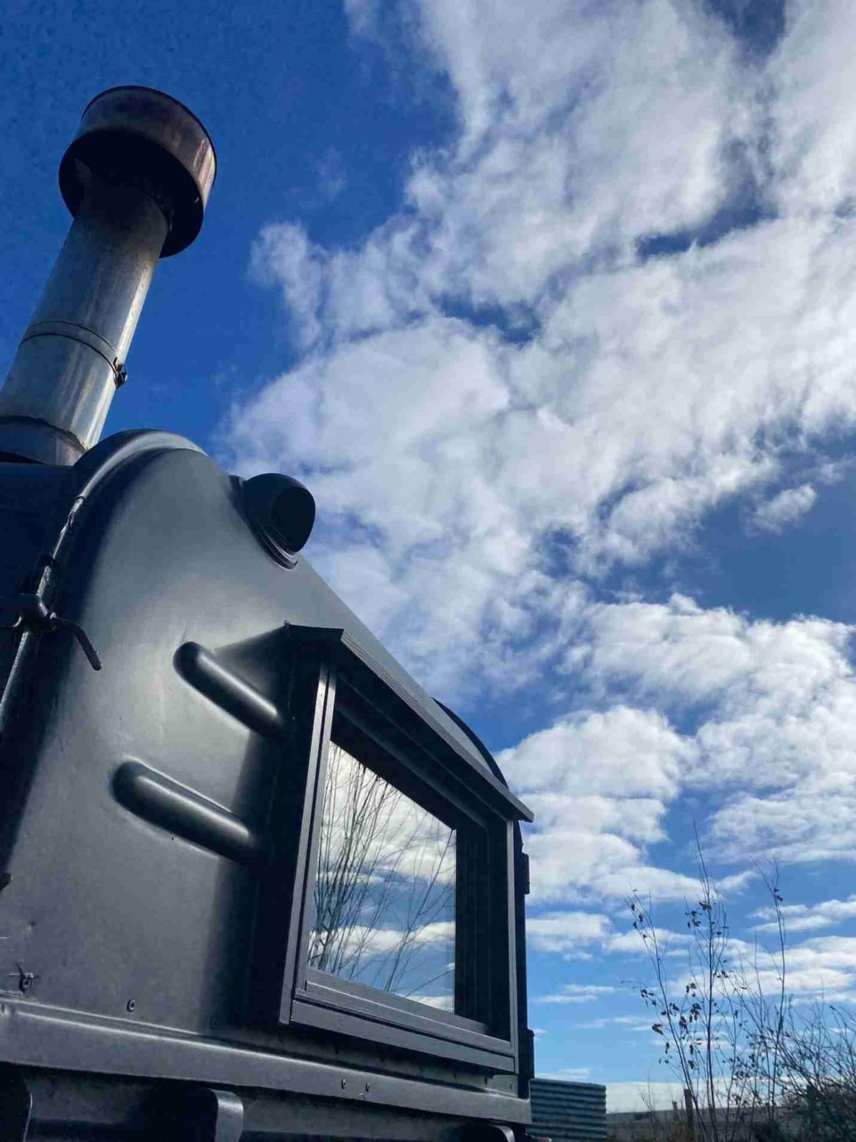 HorsA black horsebox sauna with blue sky and fluffy clouds both overhead and reflected in it's window.