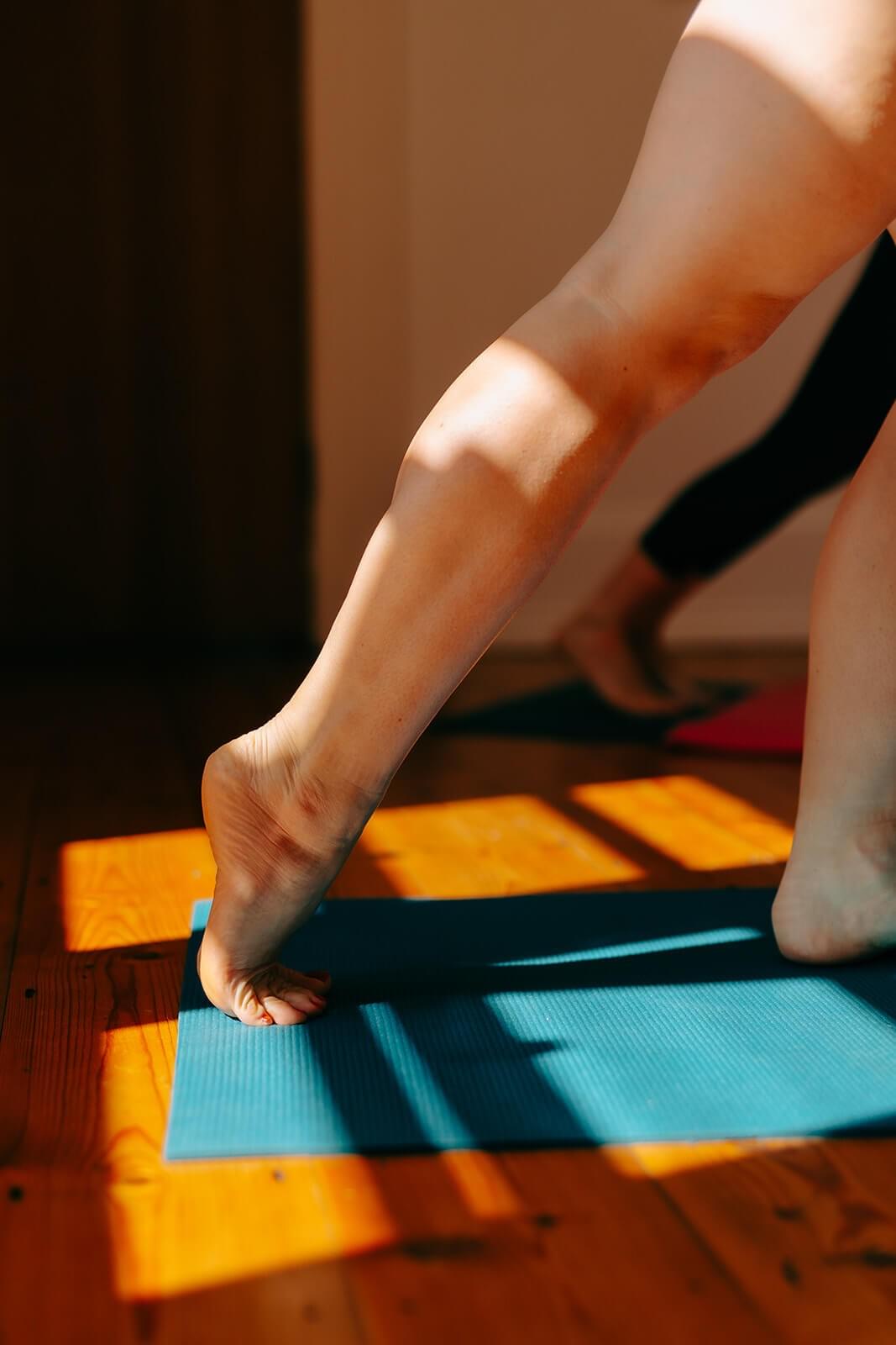 Feet on a yoga mat during an exercise session, sun streams through the window casting shadows on the wooden floor. Feet on a yoga mat during an exercise session, sun streams through the window casting shadows on the wooden floor.