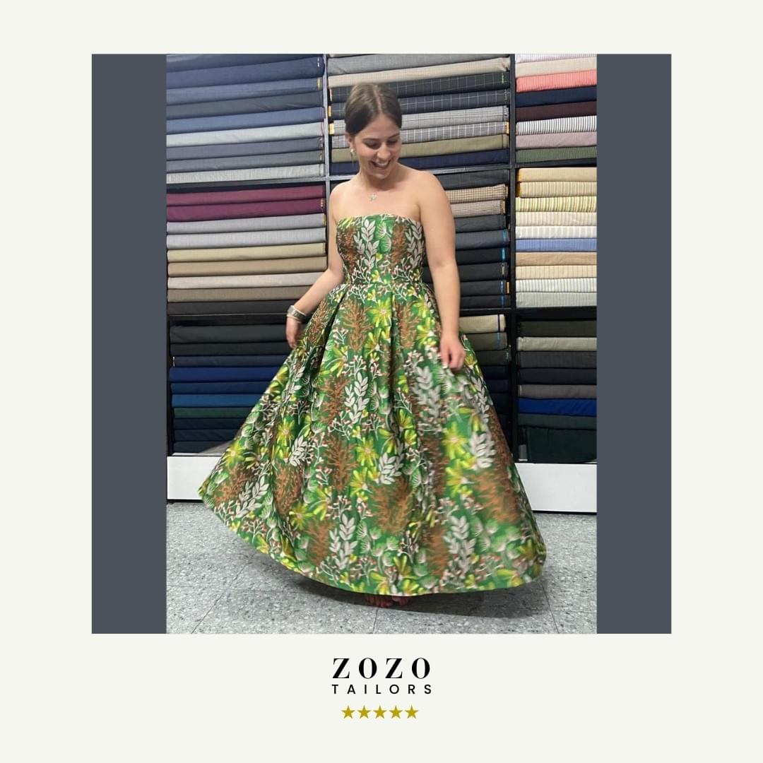 Person wearing a ball gown in satin brocade fabric, in woodland tones of green and mocha, she swirls the wid skirt. 