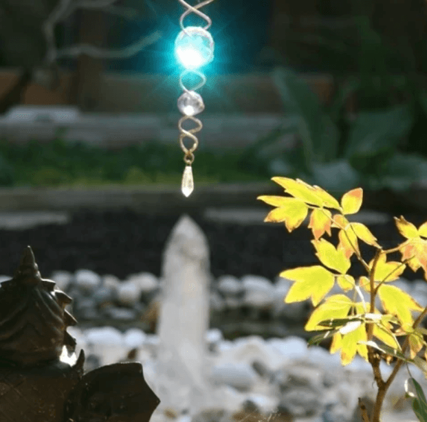 Dans un jardin, une statue de dos d'un bouddha observe un cristal et une décoration en spirale