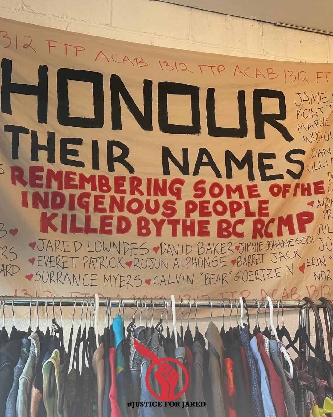 Close-up of a handpainted banner with the text "HONOUR THEIR NAMES: Remembering Some of the Indigenous People Killed by the BC RCMP." At the bottom of the image is the #JusticeForJared logo, a red fist holding an Eagle feather.