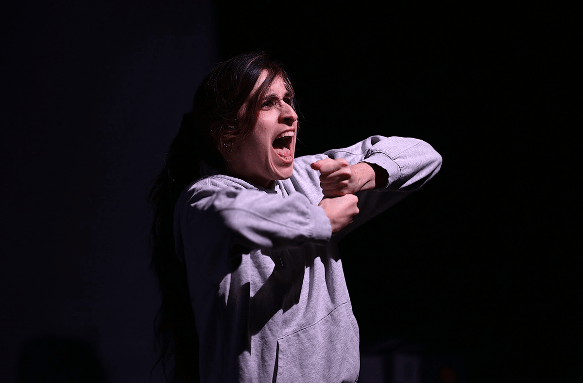 Une jeune femme tient une pancarte invisible et crie. C'est un des personnages de la pièce Lueurs. Une jeune femme tient une pancarte invisible et crie. C'est un des personnages de la pièce Lueurs.