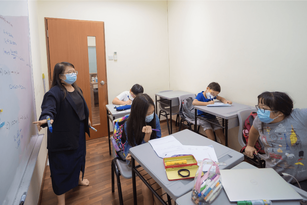 A private tutor provides one-on-one guidance to a primary school student during a tutoring session in a bright classroom or learning center.
