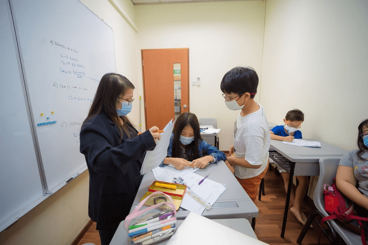 Math teacher assisting student with algebra problem at desk, personalized tutoring session in Singapore math tuition center focused on secondary school exam preparation