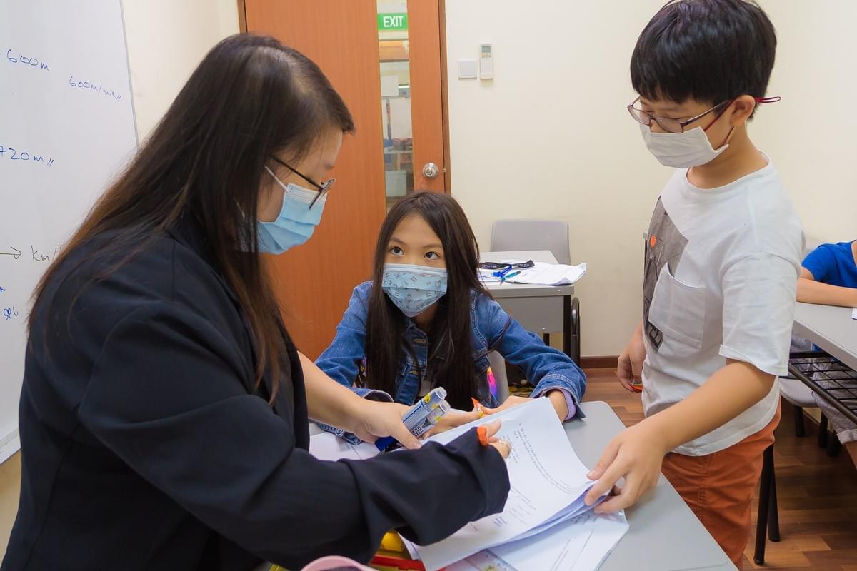 A math tutor wearing a face mask explains a quartic equation on a classroom whiteboard during a one-on-one mathematics tuition lesson.