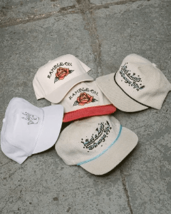Vintage-inspired embroidered snapback hats in neutral colors with floral and western-style designs displayed on a concrete surface.