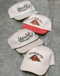 Vintage-inspired embroidered snapback hats in neutral colors with floral and western-style designs displayed on a concrete surface. Vintage-inspired embroidered snapback hats in neutral colors with floral and western-style designs displayed on a concrete surface.