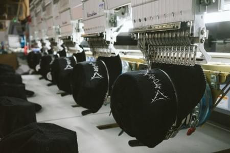 Embroidery machine stitching custom design onto black cap, highlighting precision craftsmanship and premium materials. Embroidery machine stitching custom design onto black cap, highlighting precision craftsmanship and premium materials.