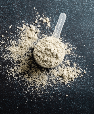 Almased scoop filled with beige nutritional powder on dark surface, emphasizing clean ingredients for balanced daily supplementation