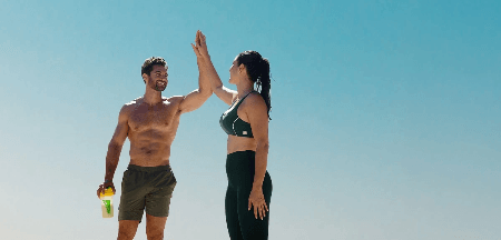 Almased two people high‑fiving outdoors with yellow shaker bottle, showcasing fitness motivation, energy and healthy active living