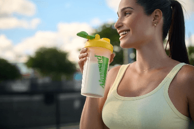 Almased person holding yellow shaker outdoors in sunny setting, highlighting daily wellness, energy and active healthy lifestyle support